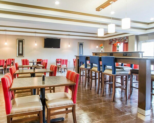 A restaurant with wooden tables and chairs, a flat-screen TV on the wall, and pendant lights.