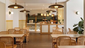 A restaurant interior with wooden tables and chairs, hanging pendant lights, and a counter with food items. - Hôtel Kemaris (Biarritz)