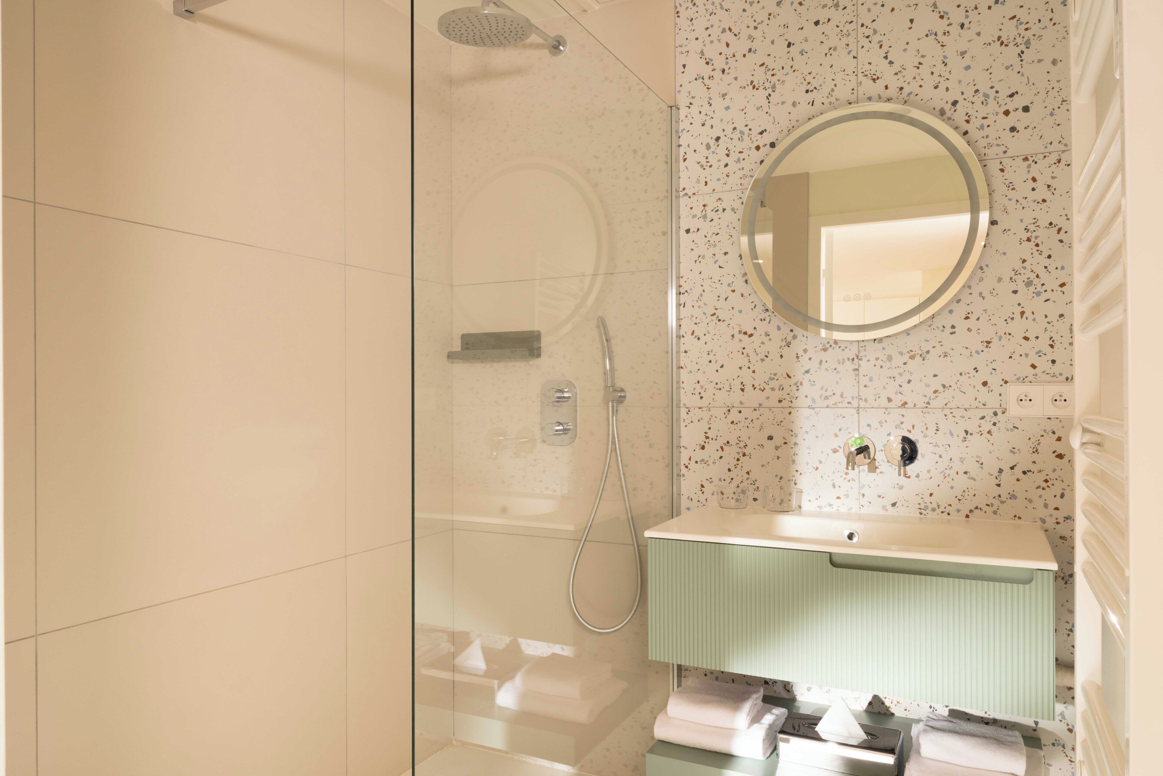 Une salle de bain moderne avec une douche à parois de verre, un miroir rond et un meuble-lavabo vert.