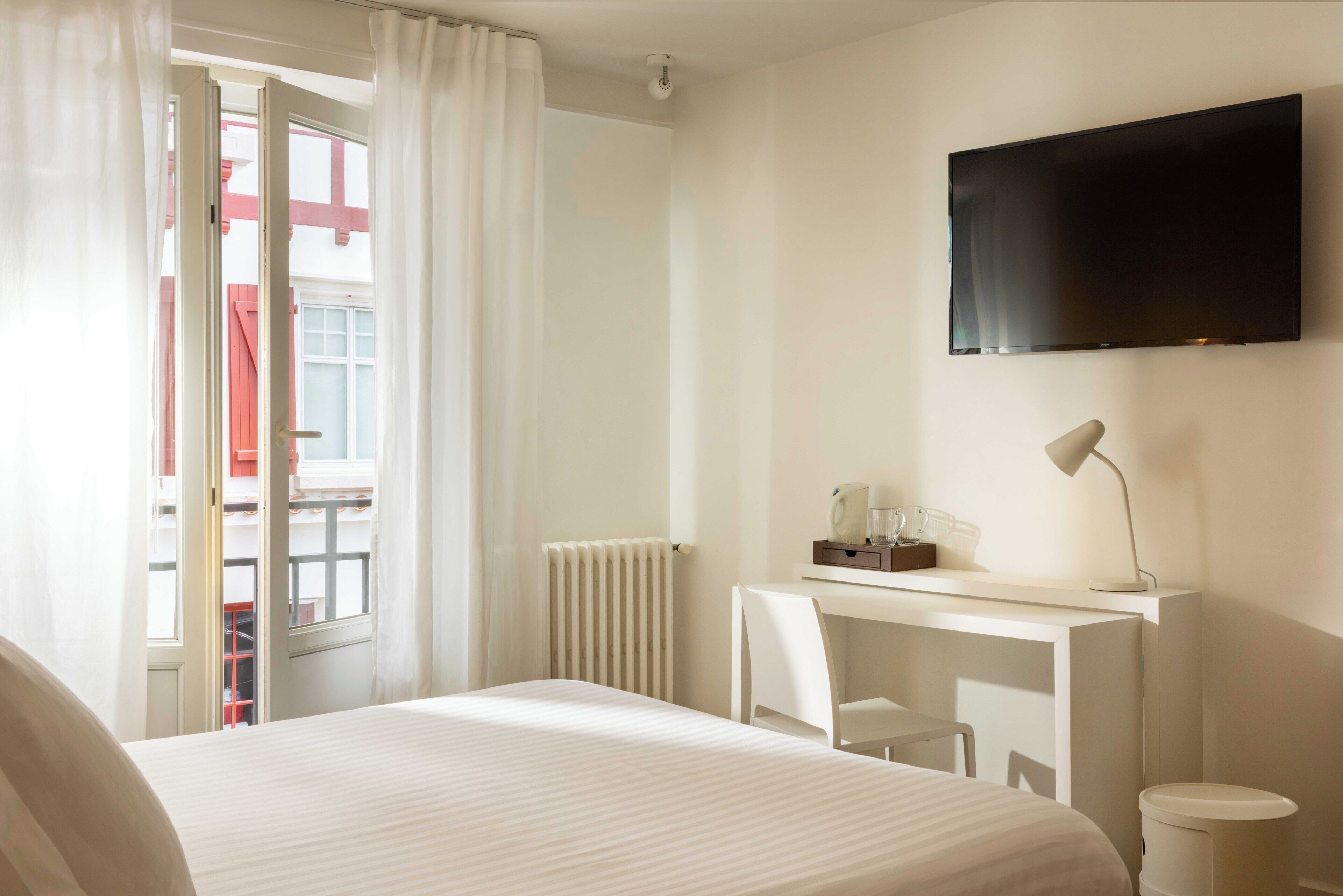 Una habitación de hotel con cama, un escritorio con silla, un televisor y un radiador.