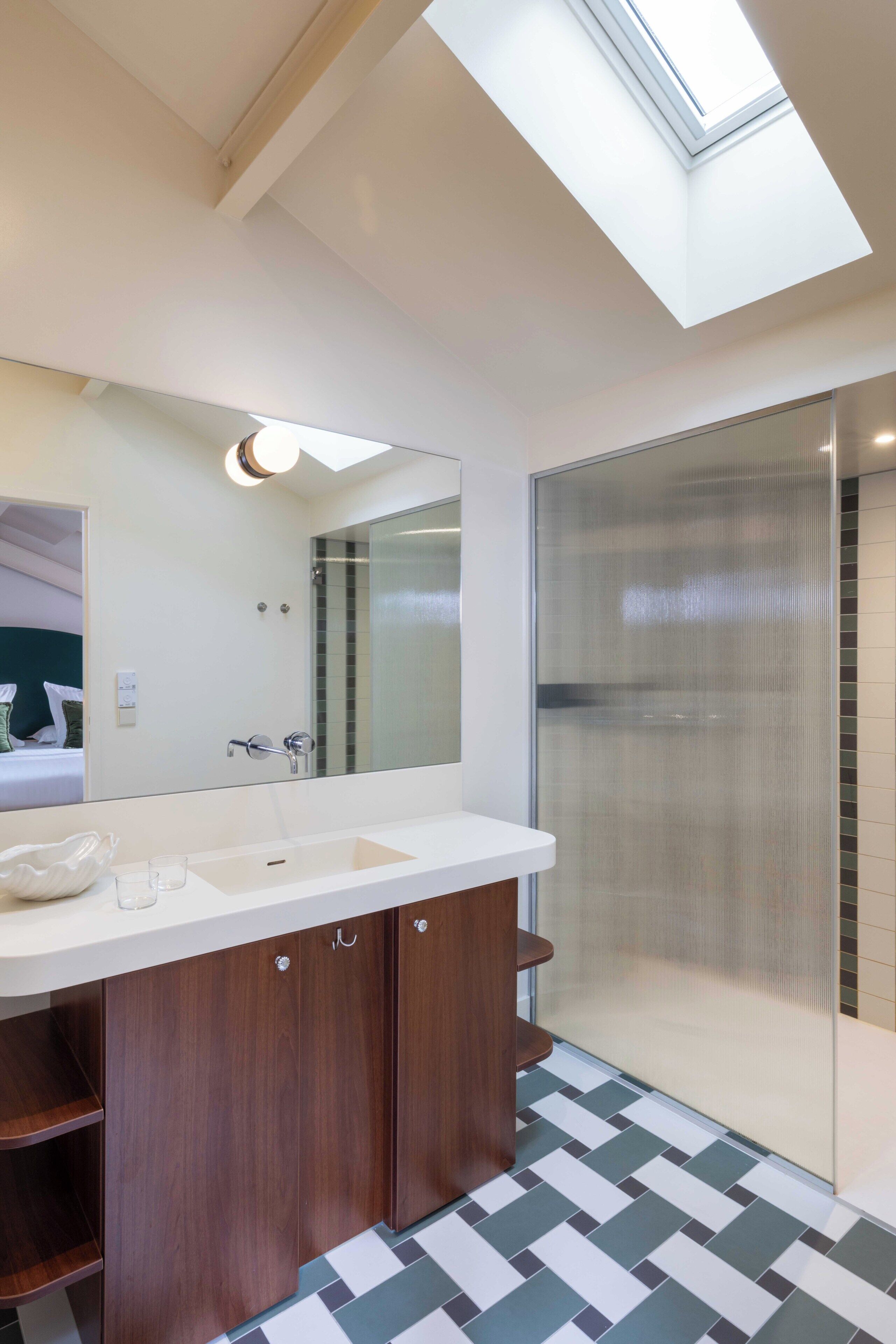 A modern bathroom with a skylight, a large mirror, a double sink, and a shower enclosure.
