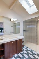 Un baño moderno con tragaluz, un espejo grande, lavamanos doble y cabina de ducha.