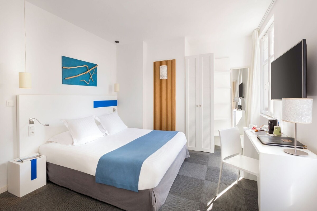A hotel room with a bed, bedside table, desk, chair, TV, and a wardrobe.