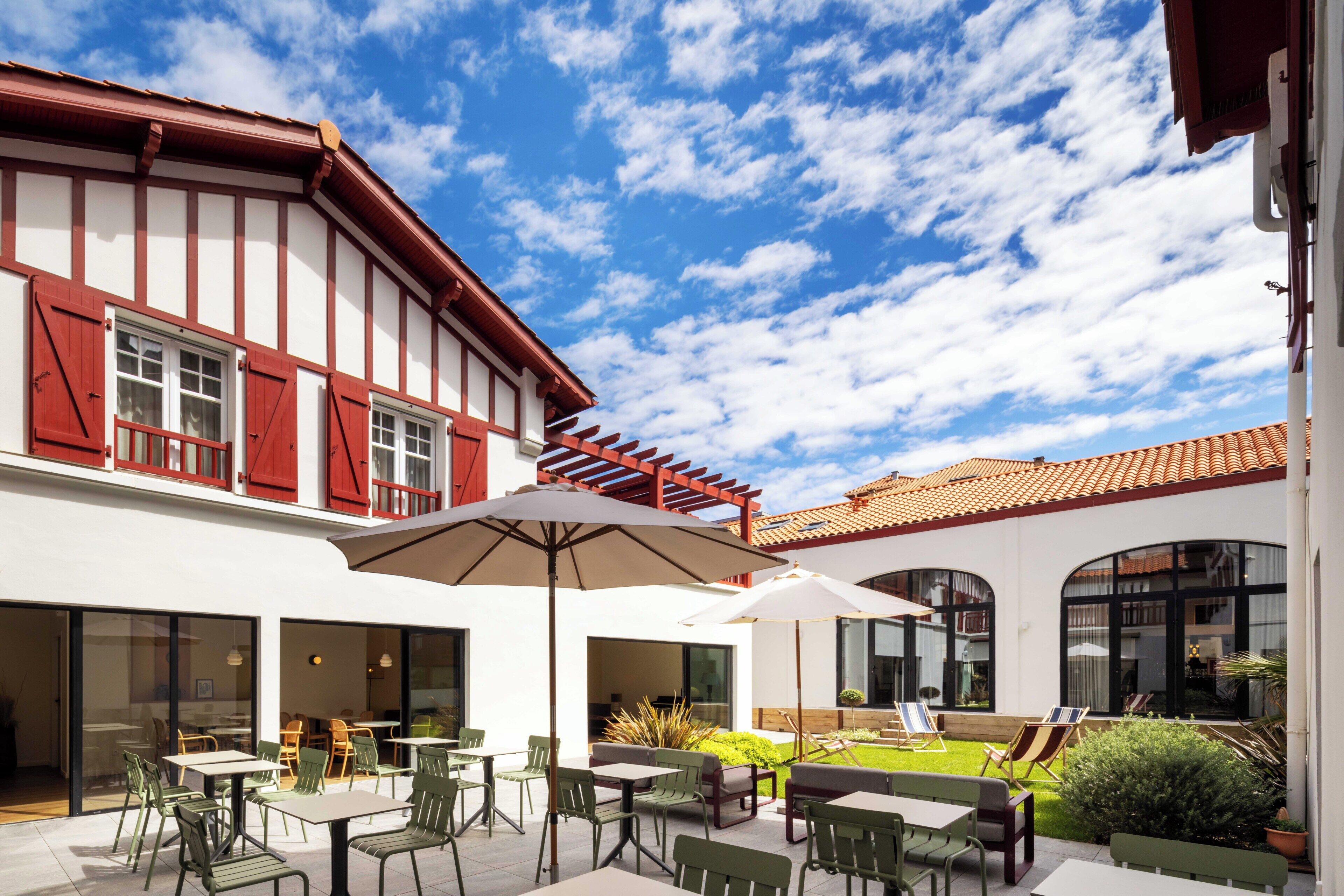A courtyard with outdoor seating, a pergola, and a building with a red and white facade.