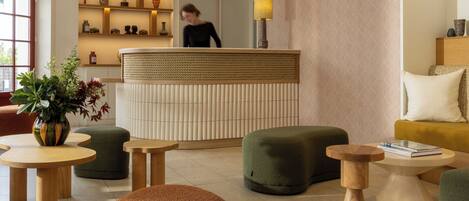 A modern hotel lobby with a reception desk, seating areas, and a large window.