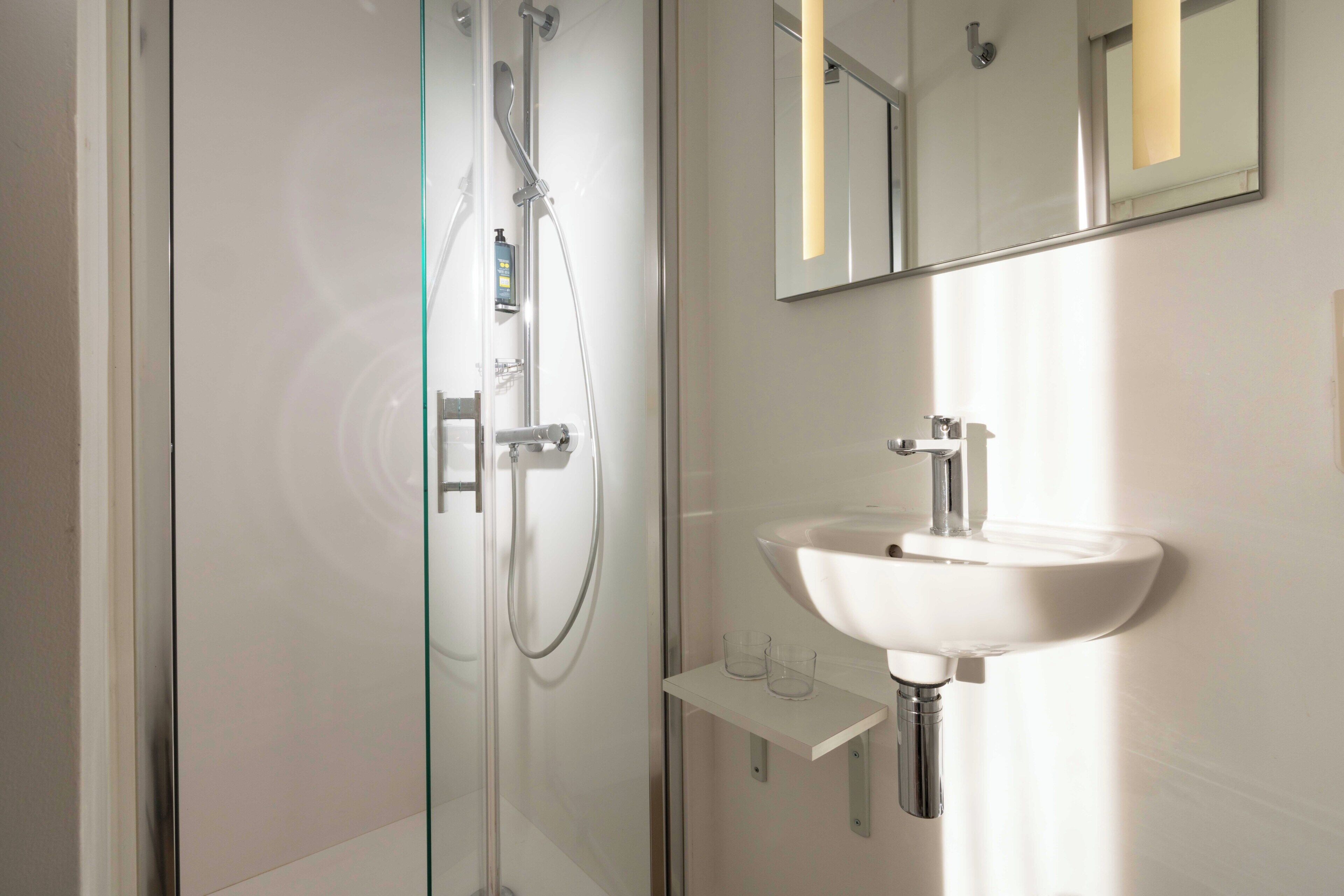 A modern bathroom with a glass shower enclosure, a white sink, and a mirror above the sink.