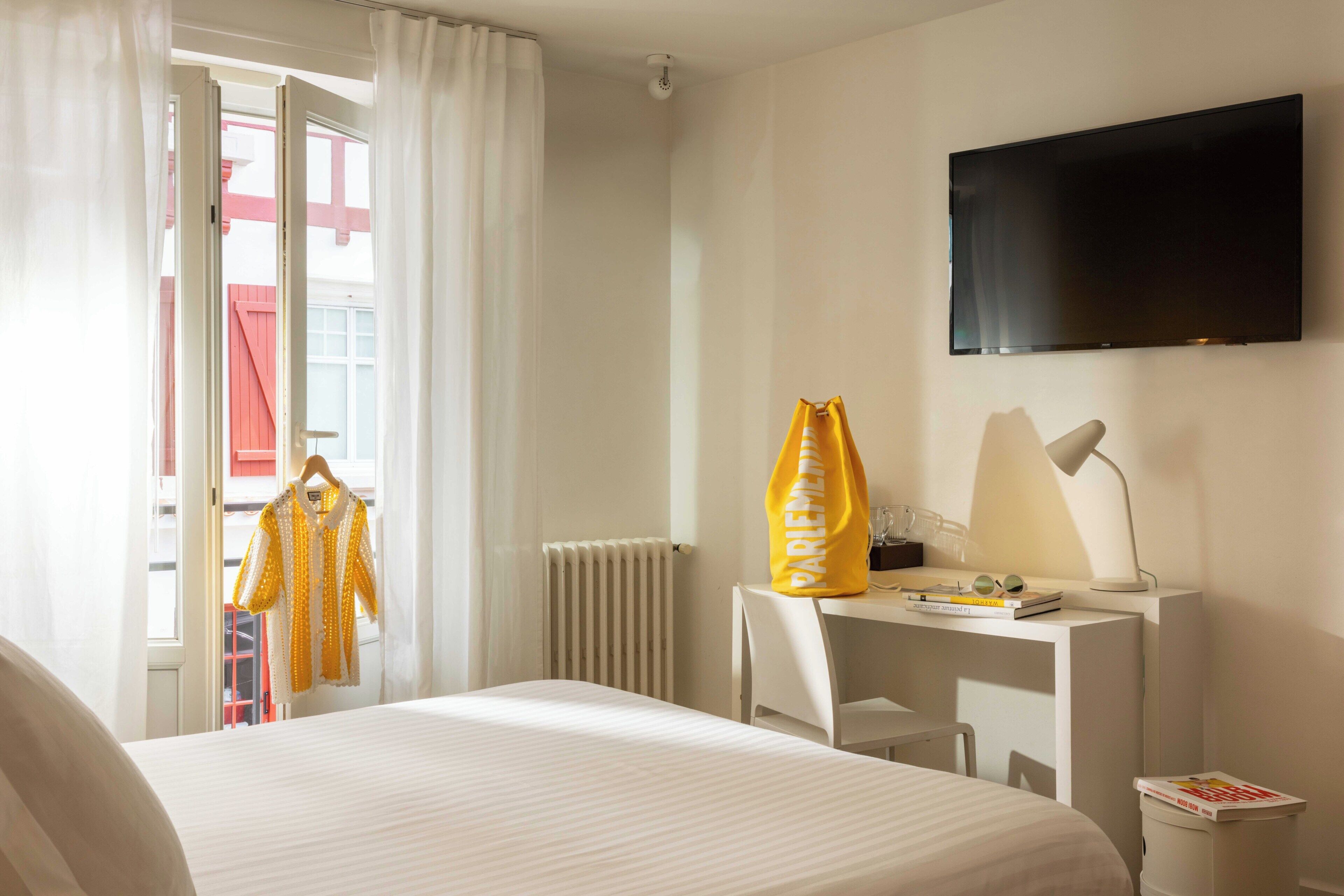 Une chambre d’hôtel avec un lit, un bureau et une chaise, une télévision et une fenêtre avec des rideaux.