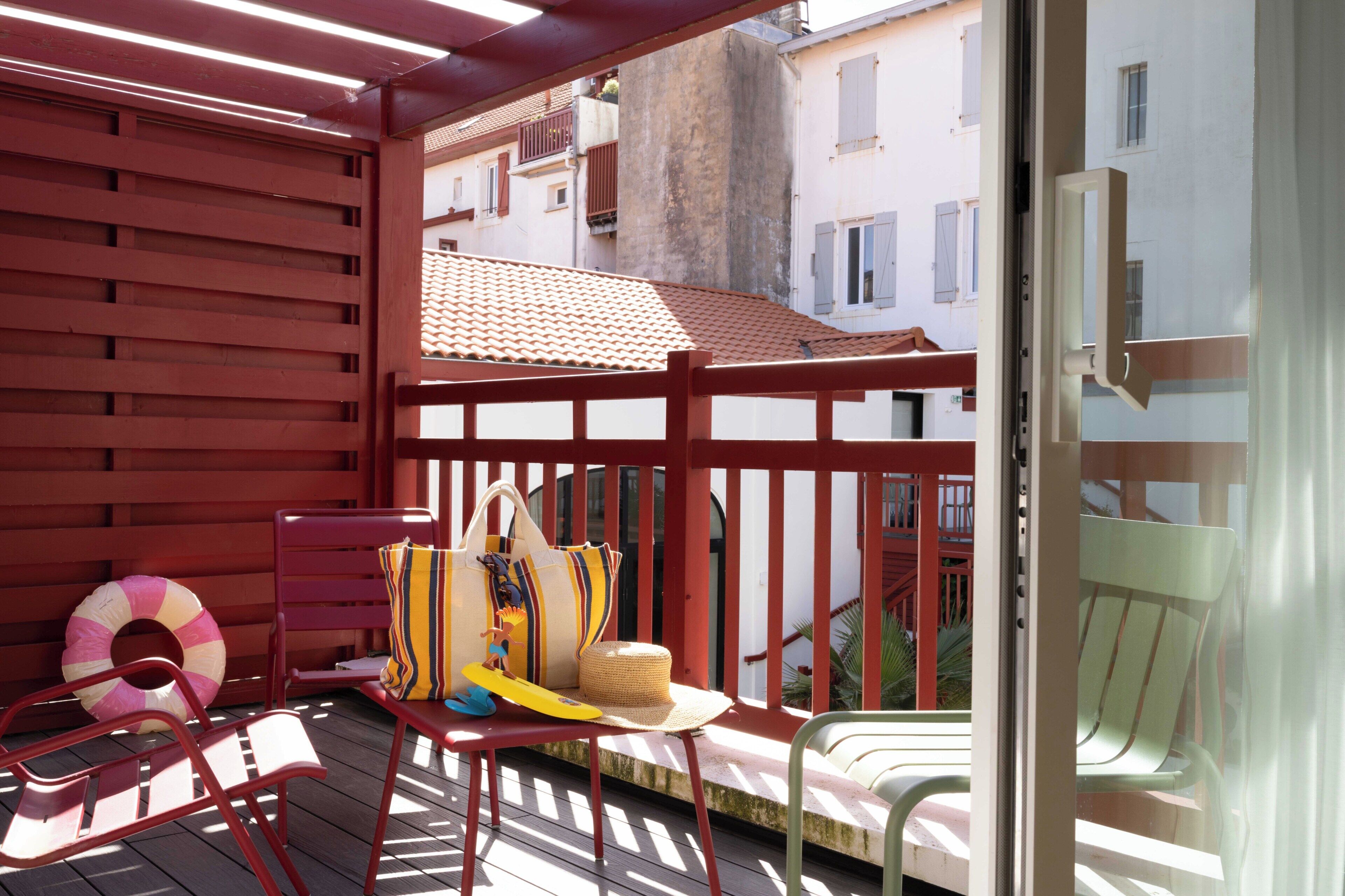 Eine Holzterrasse mit roten Geländern, einem Liegestuhl, einer Sonnenliege und einem Strandtuch.