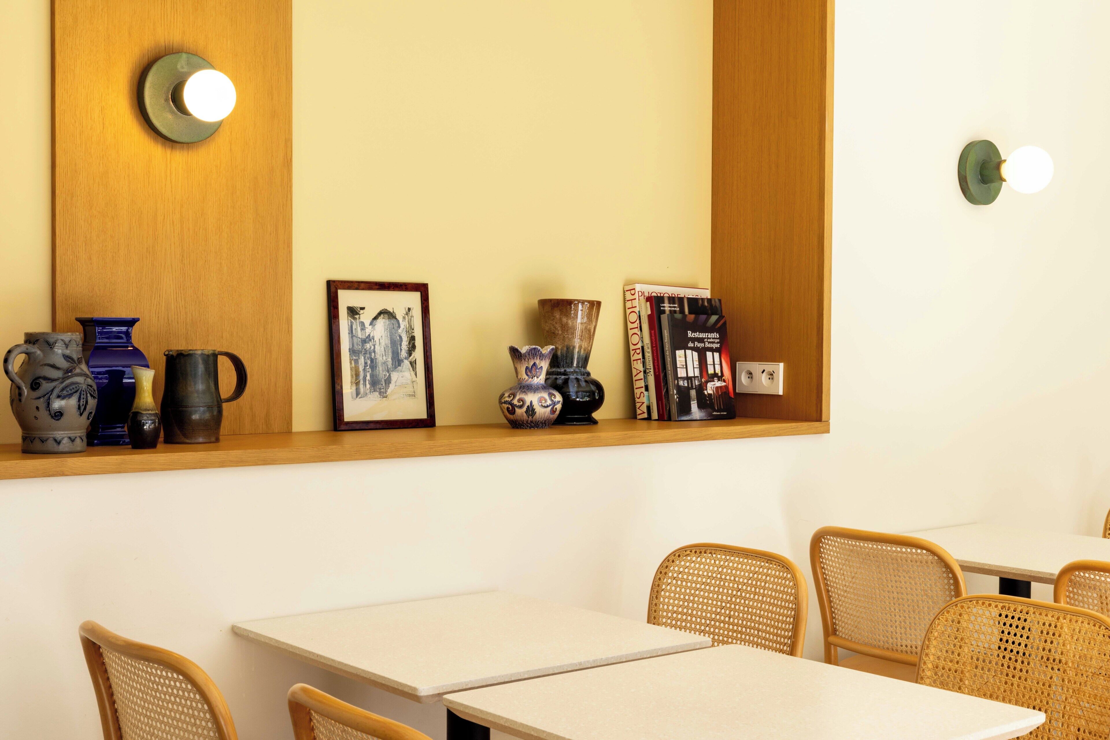 A dining area with tables and chairs, a shelf with decorative items, and wall-mounted light fixtures.