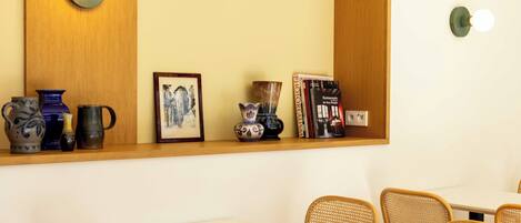 A dining area with tables and chairs, a shelf with decorative items, and wall-mounted light fixtures.