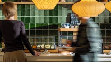 A counter with a display case containing food items, a chalkboard menu, and a person serving.