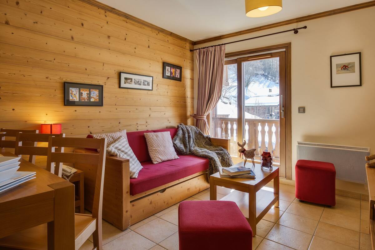 Ein gemütliches Zimmer mit Holzwand, einem roten Sofa, einem Holztisch und einem roten Hocker.