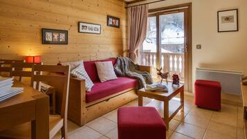 Une pièce chaleureuse avec un mur en bois, un canapé rouge, une table en bois et un pouf rouge.