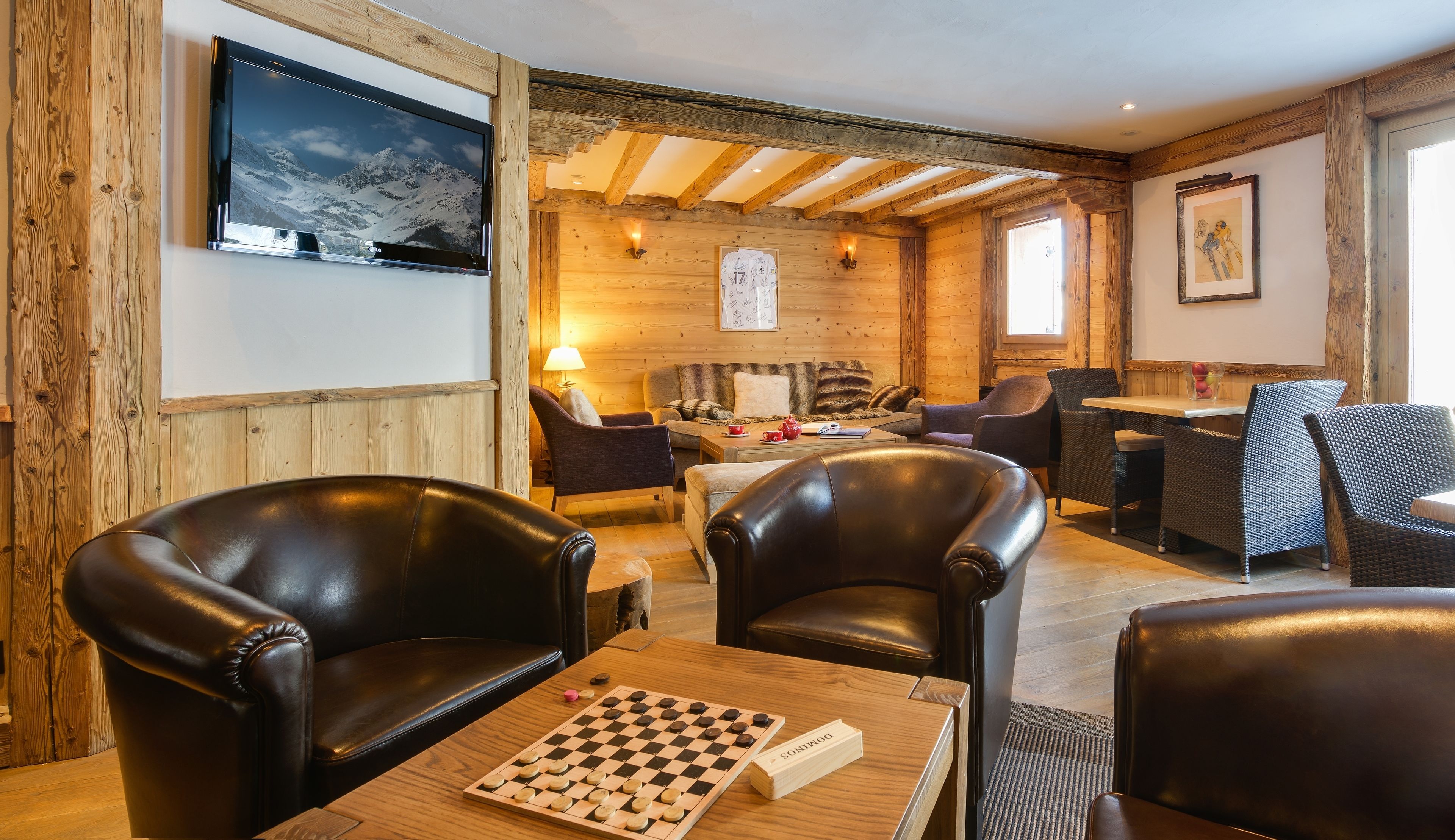 Une pièce chaleureuse aux murs en bois, avec une cheminée, un téléviseur fixé au mur et un jeu d’échecs posé sur une table.