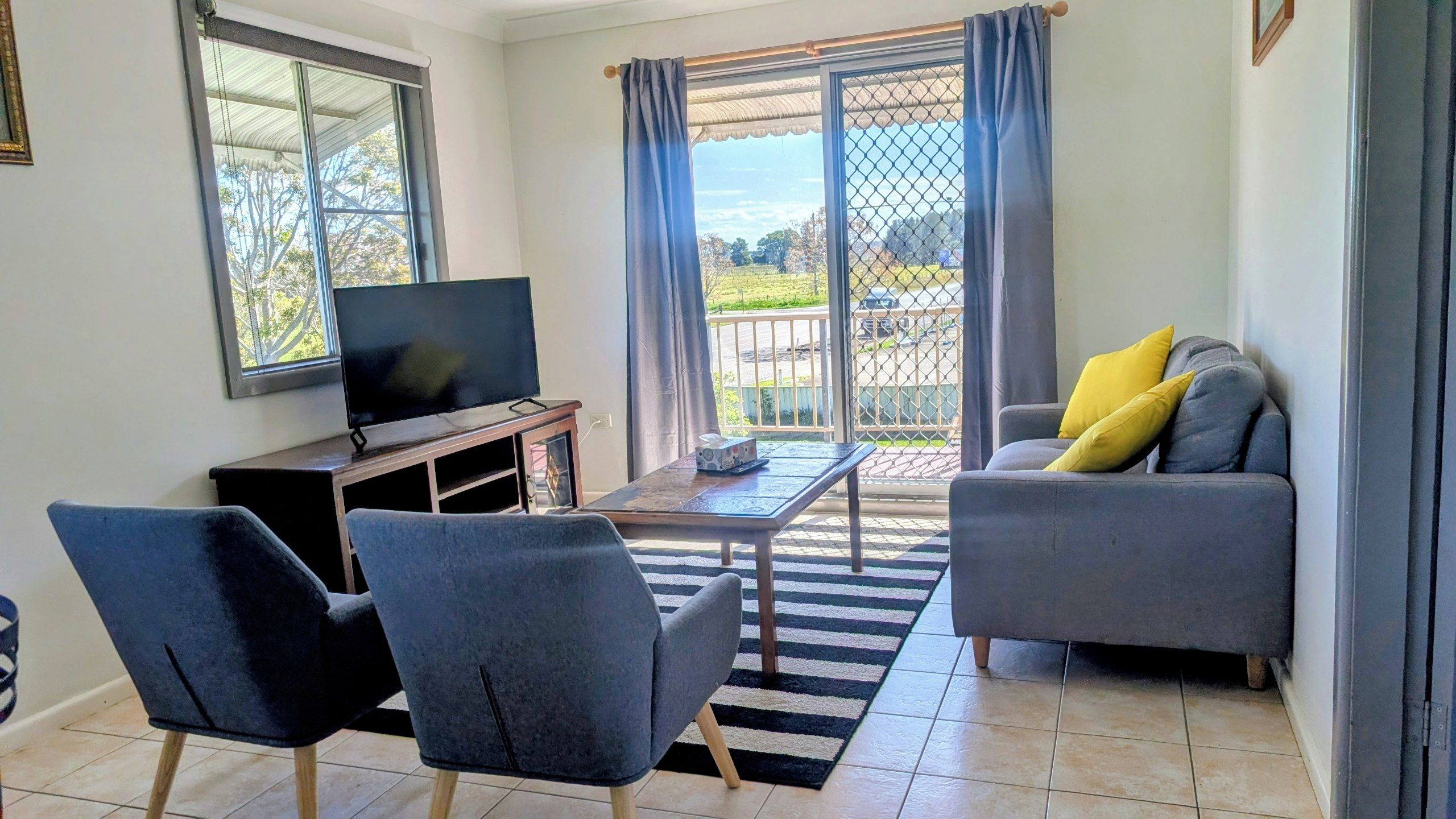 A living room with a TV, two chairs, a sofa, and a view through a sliding door.