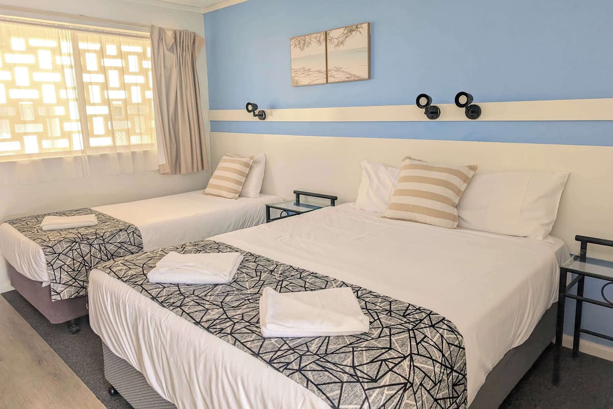 A hotel room with two beds, a window with curtains, a wall-mounted artwork, and a bedside table.