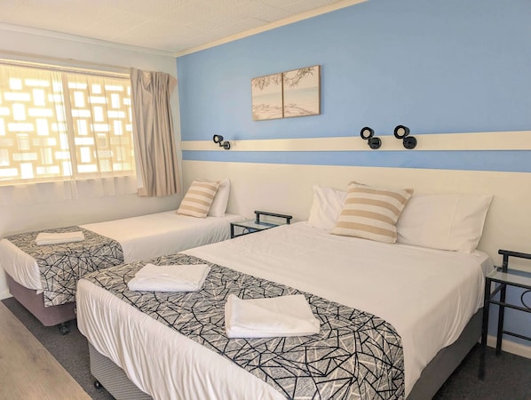Habitación de hotel con dos camas, una ventana con cortinas, una obra de arte colgada en la pared y una mesita de noche.