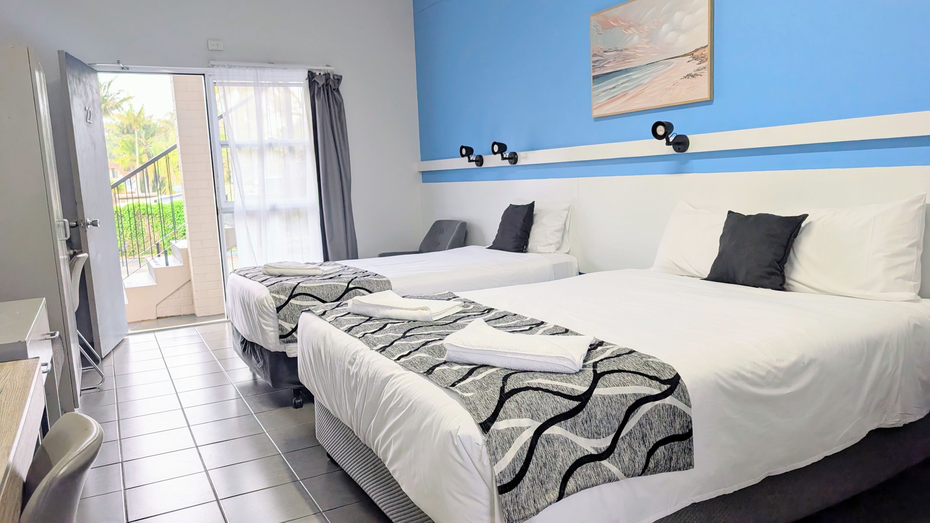 A hotel room with two beds, a balcony, and a painting on the wall.