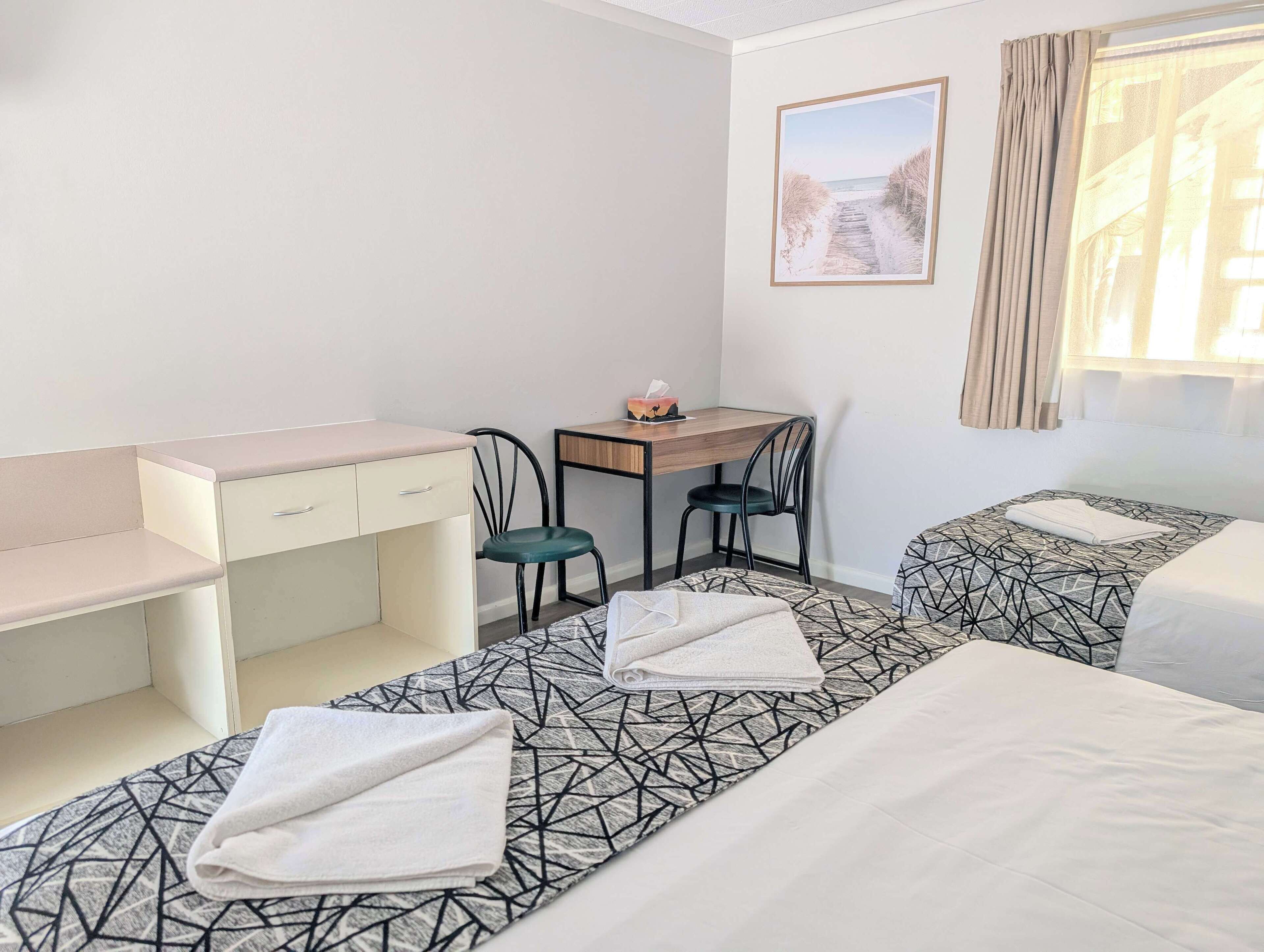 Quarto de hotel com duas camas, uma escrivaninha e uma cadeira.