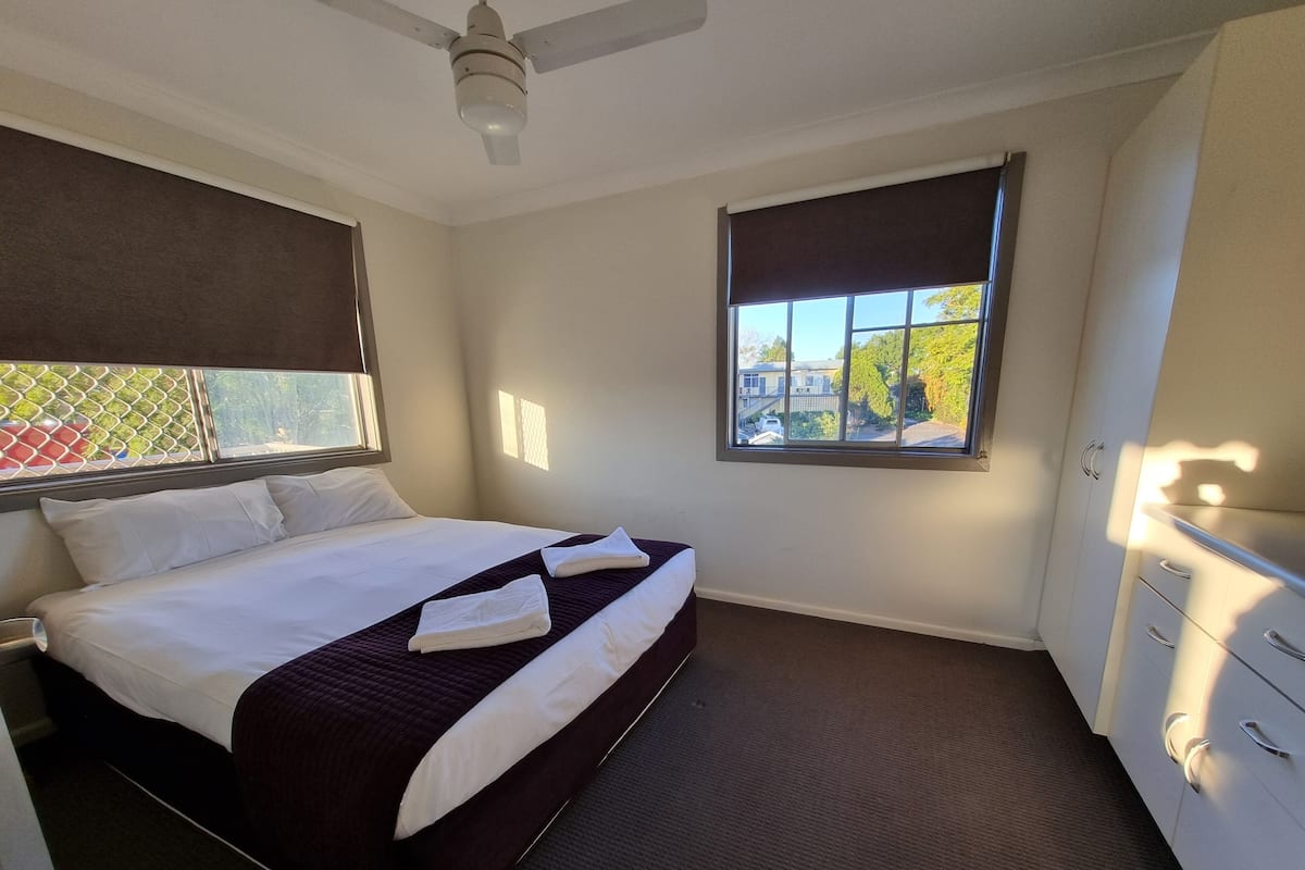 A hotel room with a bed, a window with a view, a ceiling fan, and a wardrobe.