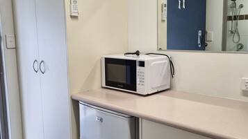 Una kitchenette con microondas, un refrigerador pequeño y un mueble con un espejo arriba.