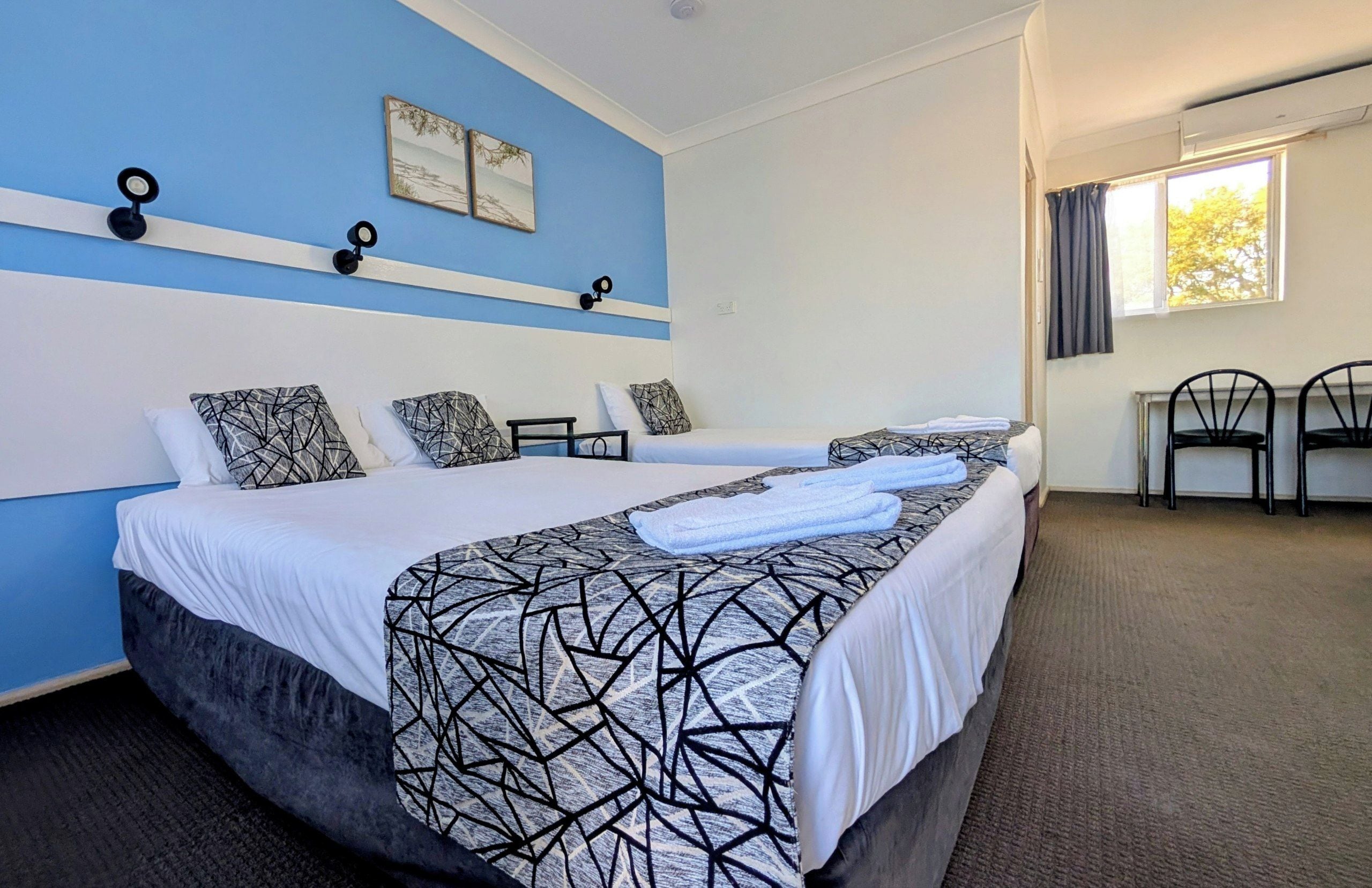 A hotel room with two beds, a desk, and a chair.
