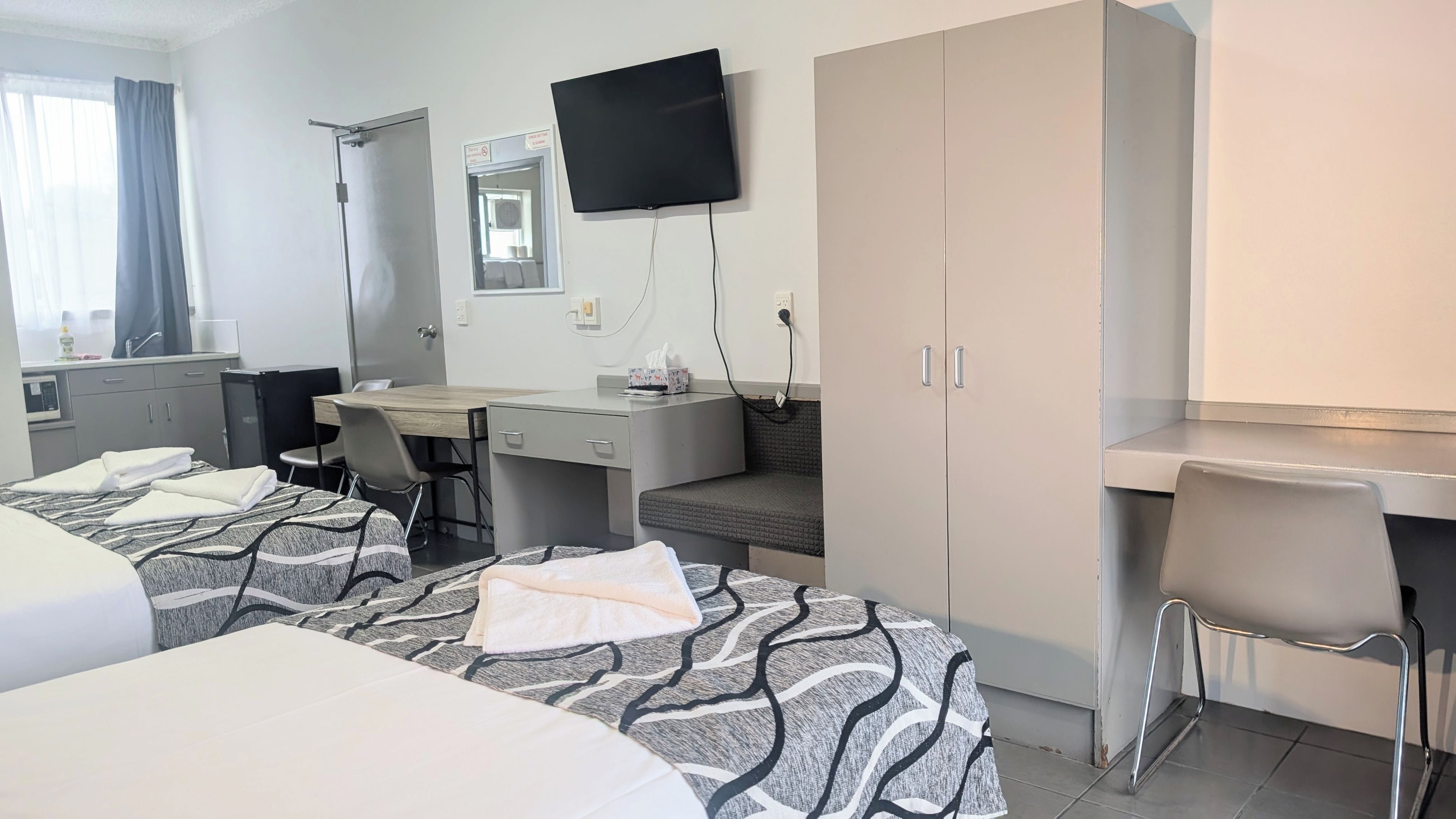 A hotel room with two beds, a desk, a chair, a television, and a bathroom.