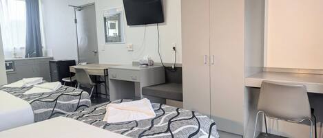 A hotel room with two beds, a desk, a chair, a television, and a bathroom.