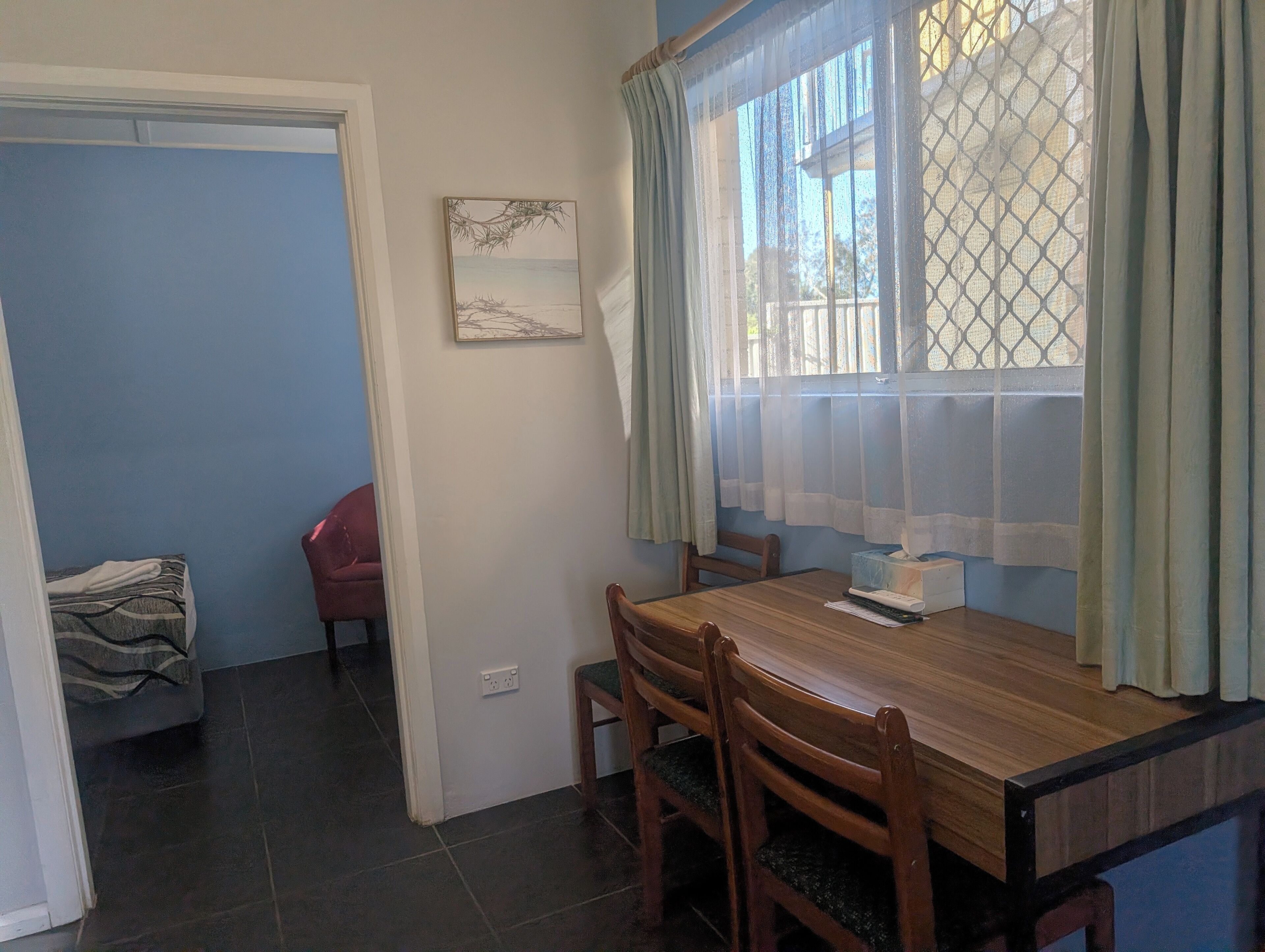 A dining area with a wooden table, chairs, a window with curtains, and a wall-mounted picture.