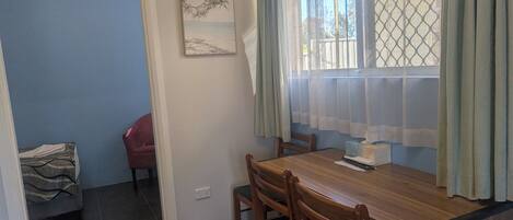 A dining area with a wooden table, chairs, a window with curtains, and a wall-mounted picture.