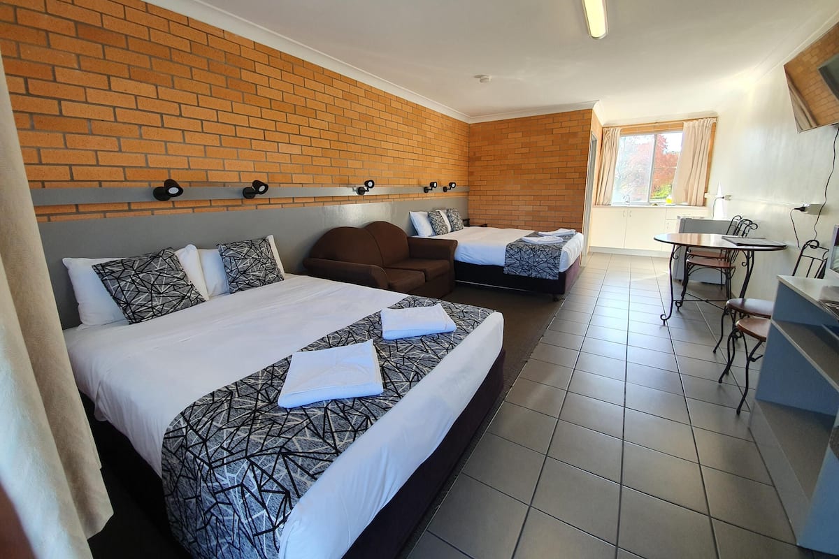 A hotel room with two beds, a sofa, a dining area, and a brick wall.