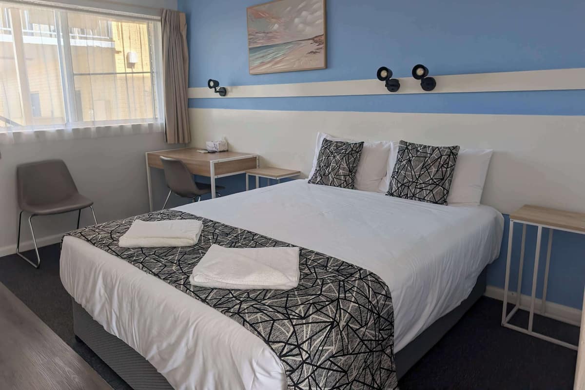 A hotel room with a bed, a desk, a chair, and a window with curtains.
