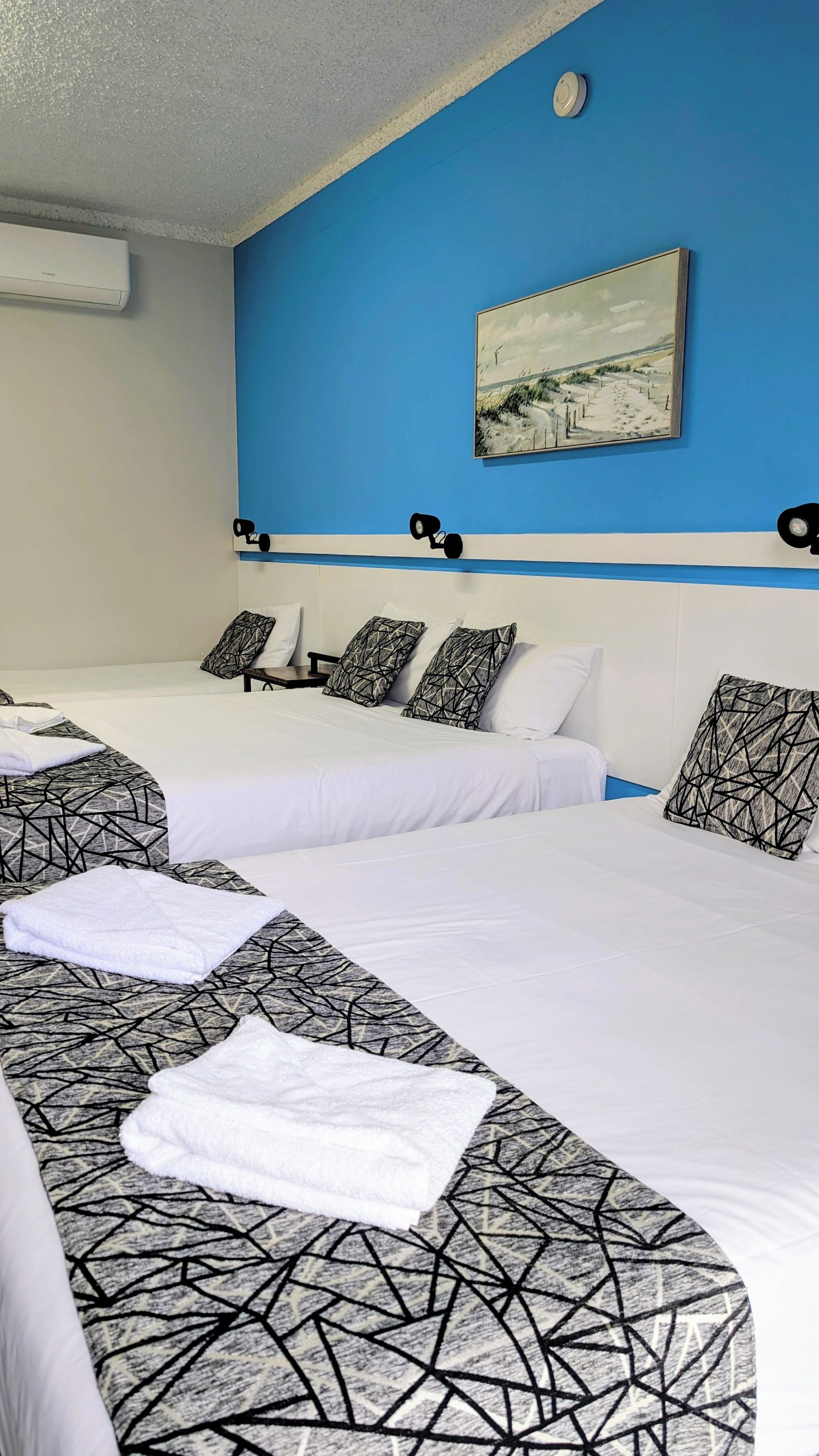 Une chambre d’hôtel avec deux lits, un tableau au mur et un ventilateur de plafond.