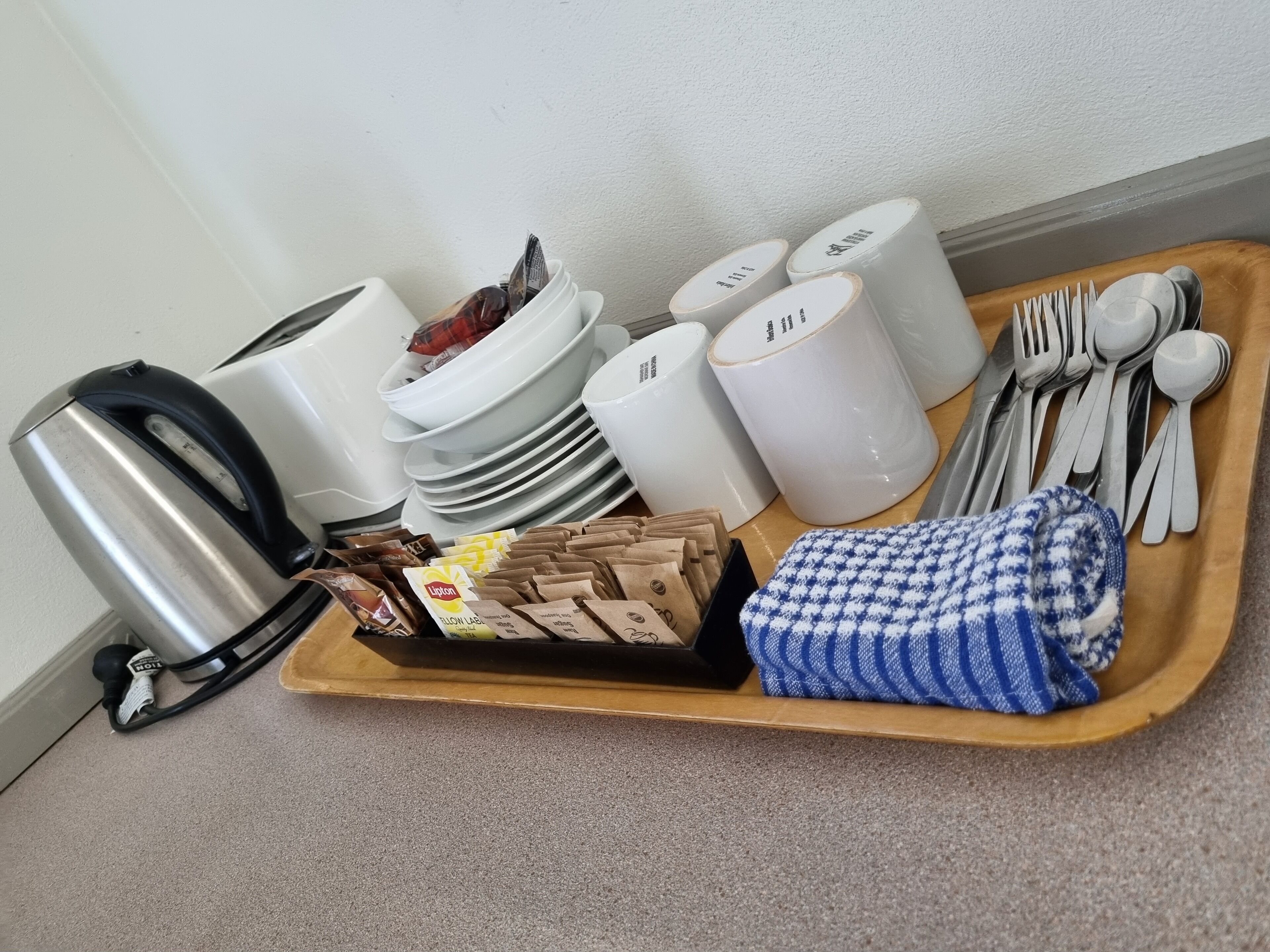 Un plateau contenant des ustensiles de cuisine, notamment une bouilloire, des assiettes, des bols, des couverts et des essuie-tout en papier.