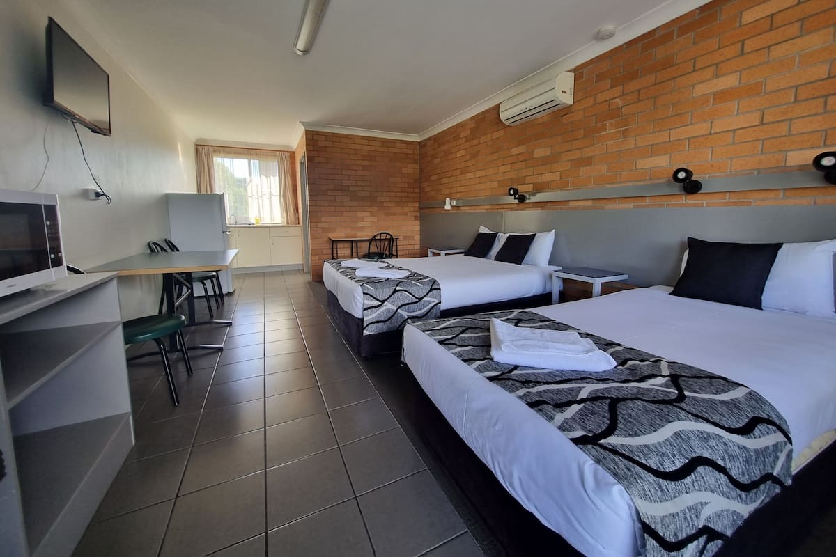 A hotel room with two beds, a desk with a chair, a TV, and a brick wall.
