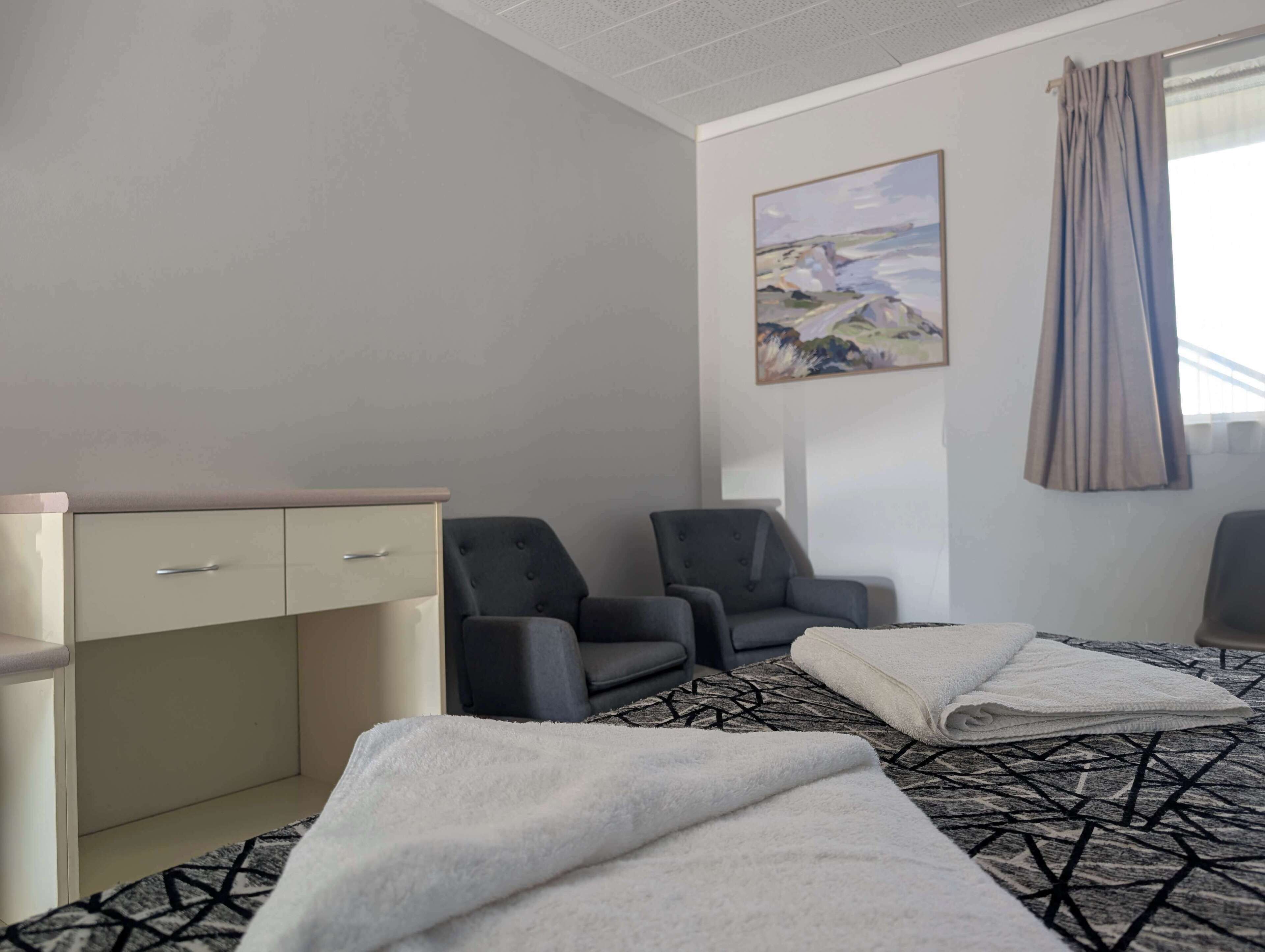 A hotel room with a bed, two chairs, a desk, and a painting on the wall.
