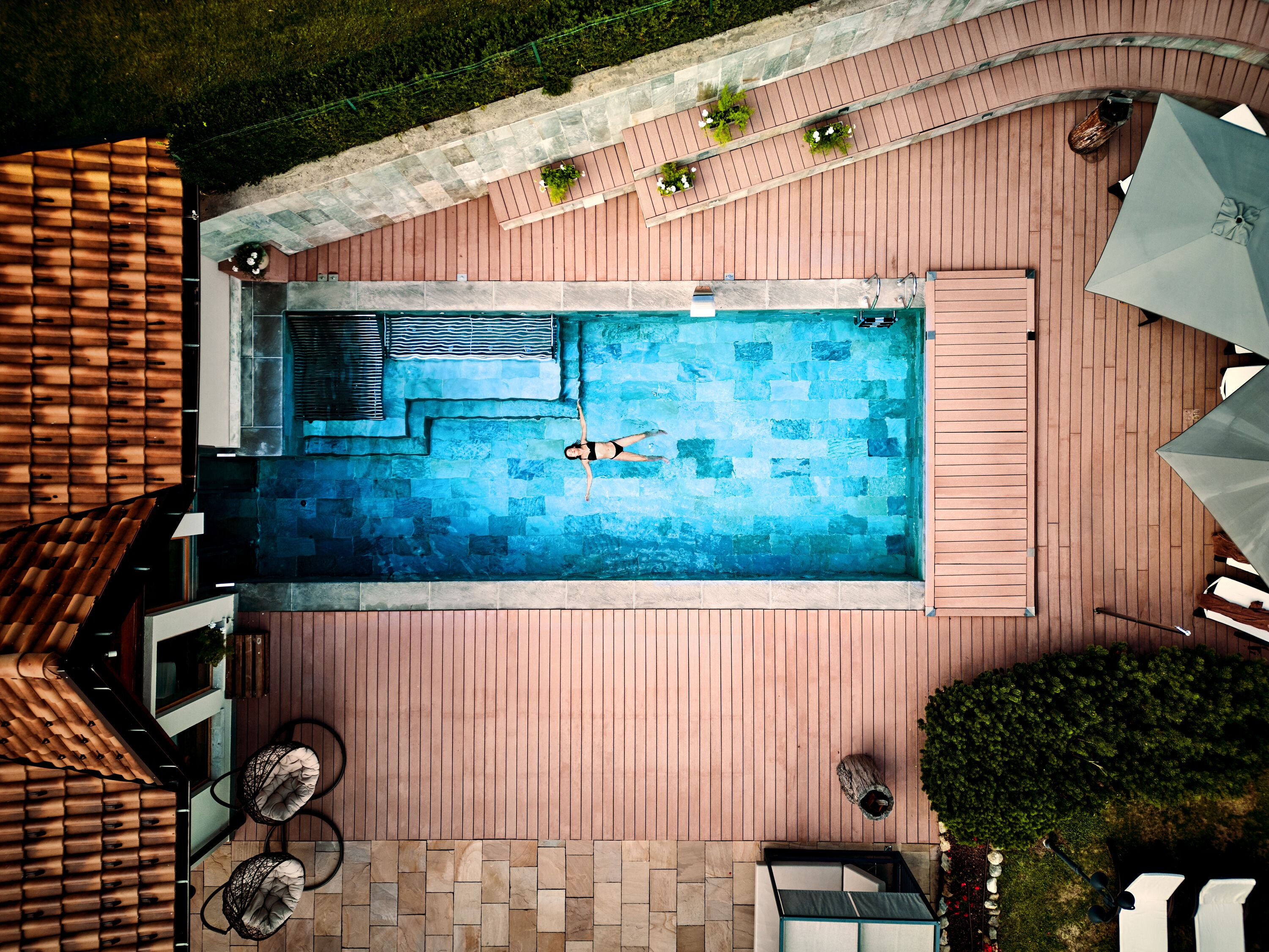 A rectangular swimming pool with a tiled deck, surrounded by wooden decking and a covered seating area.