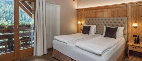 A double bed with a wooden headboard, a nightstand with a lamp, and a view of a forest through a sliding glass door.