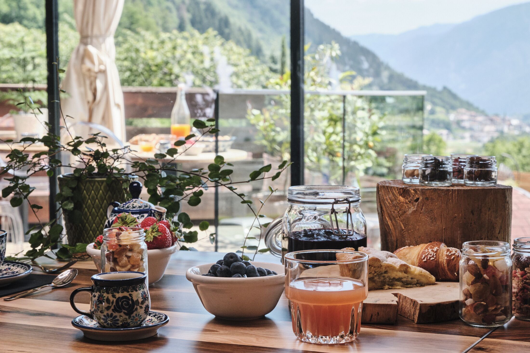 Une table de petit-déjeuner garnie de divers aliments, un verre de jus d’orange et, en arrière-plan, une vue imprenable sur les montagnes.