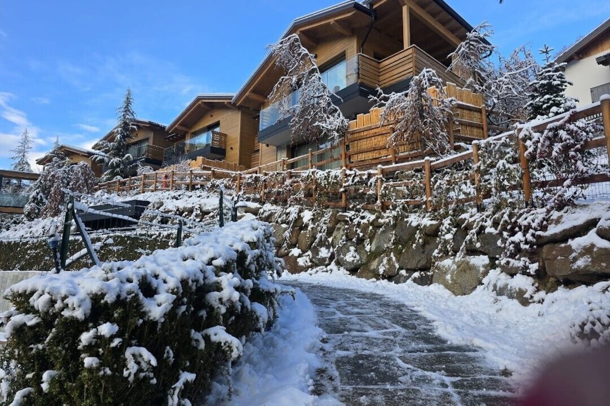 Un chalet enneigé, avec un sentier de pierres menant à l’entrée.