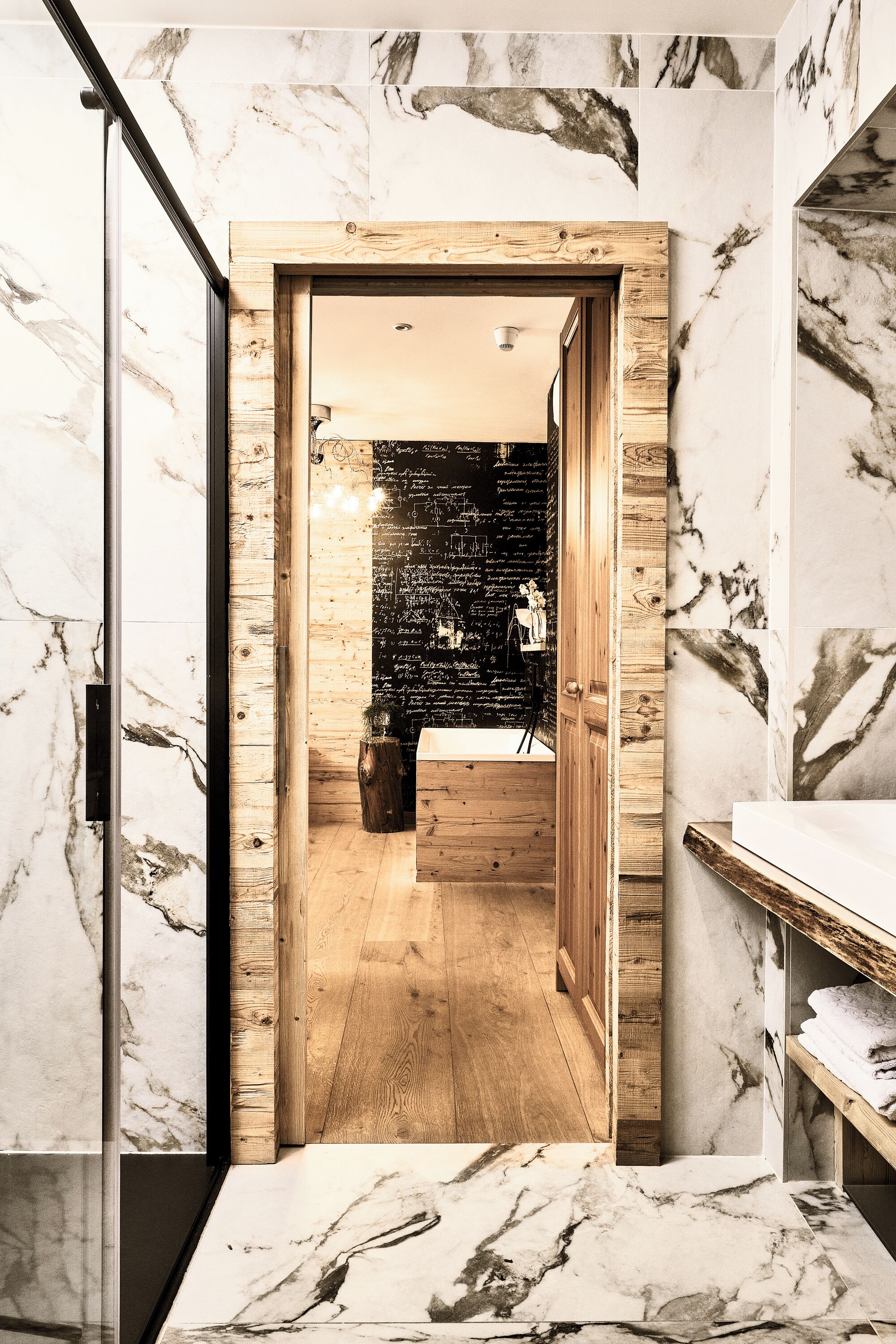 A modern bathroom with marble walls, a wooden door, and a visible sink area.