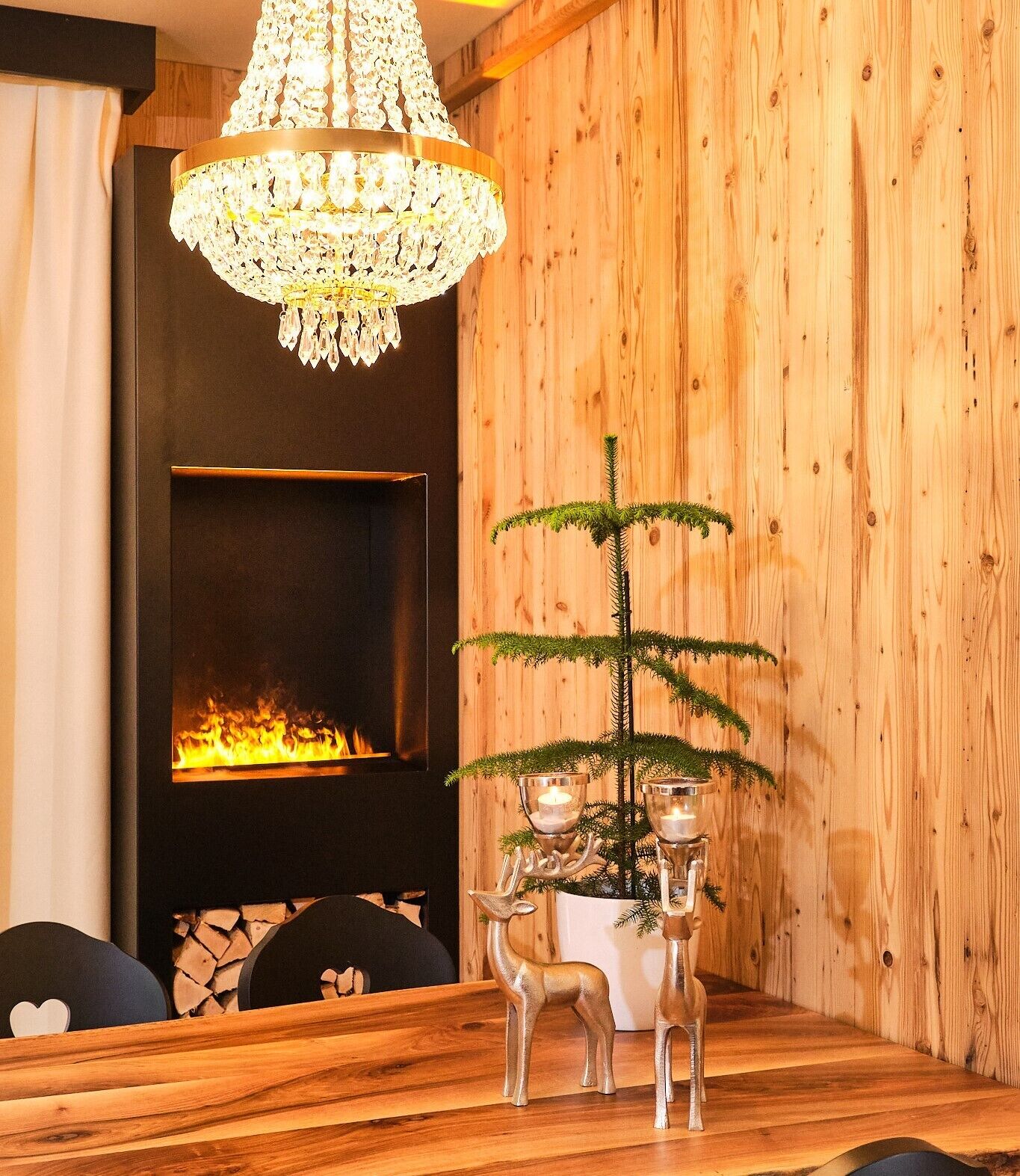 Un tavolo da pranzo in legno con un lampadario, un camino e una pianta decorativa con candele.