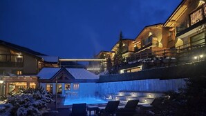Un espacio exterior cubierto de nieve con una piscina climatizada, sillas de descanso y un edificio con fachada de vidrio.
