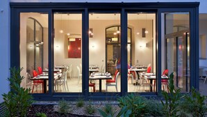 A modern restaurant with glass walls, red chairs, and a well-lit interior. - Red and Blue Design Hotel Prague (Prague)