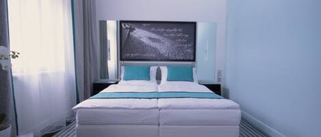 Habitación de hotel moderna con una cama grande, un televisor de pantalla plana en la pared y una planta en maceta a la izquierda.