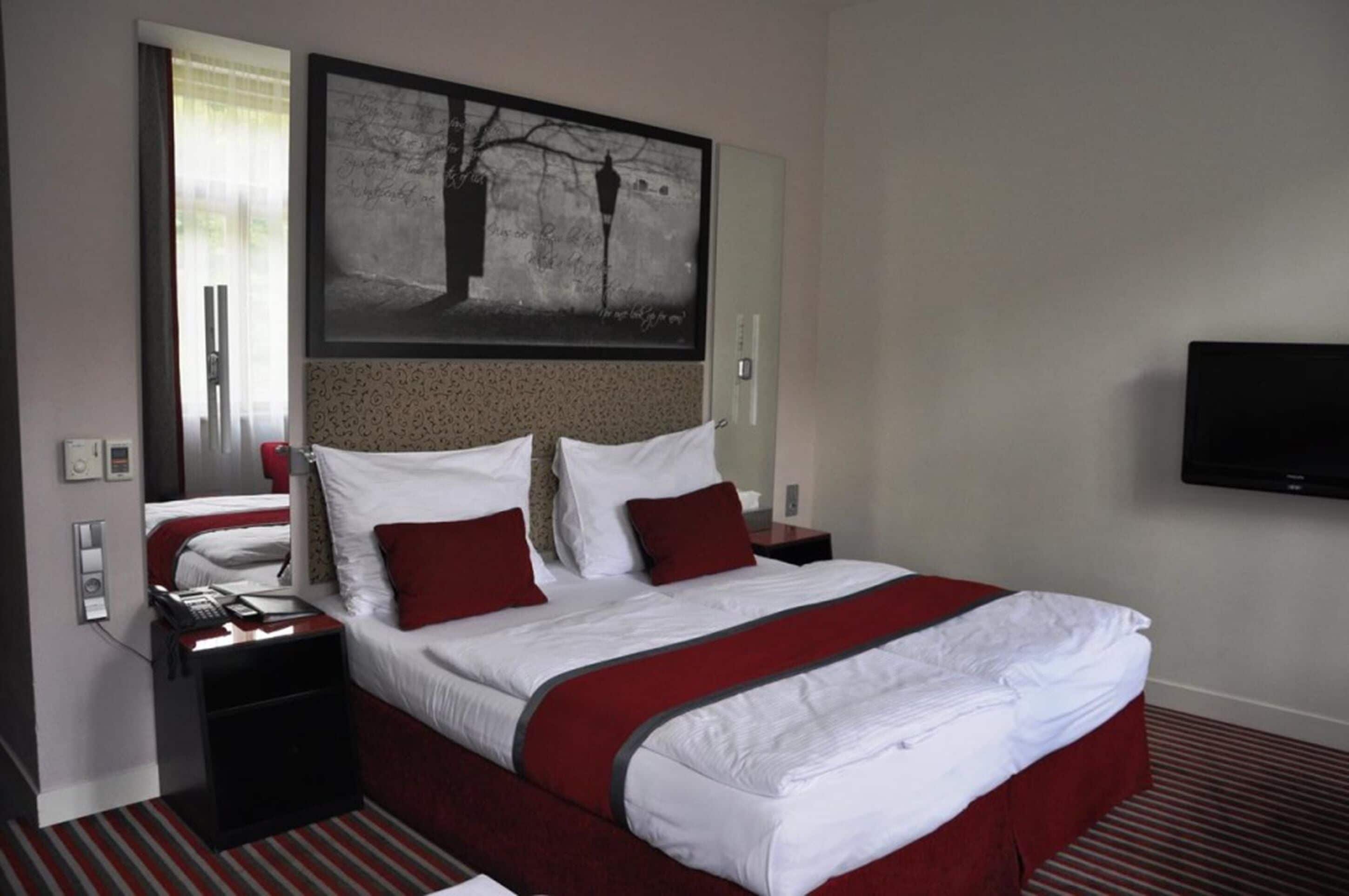 A hotel room with a large bed, a flat-screen TV mounted on the wall, and a window with curtains.
