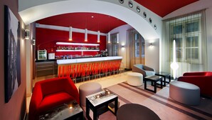 A modern bar area with a red and white color scheme, bar stools, and a seating area with red and grey furniture. - Red and Blue Design Hotel Prague (Prague)