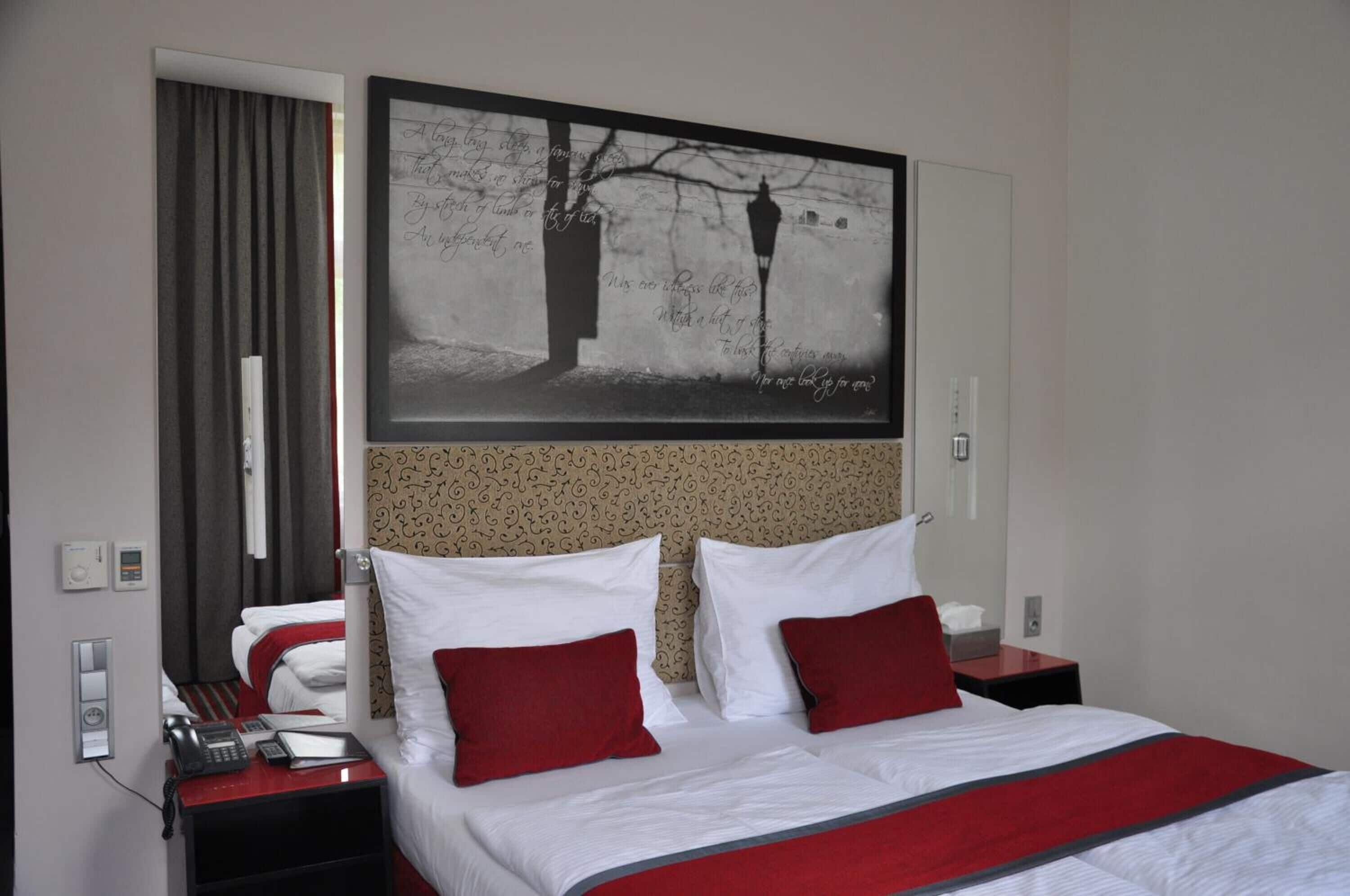 A hotel room with a bed, a telephone, a nightstand, a mirror, and a wall-mounted artwork.