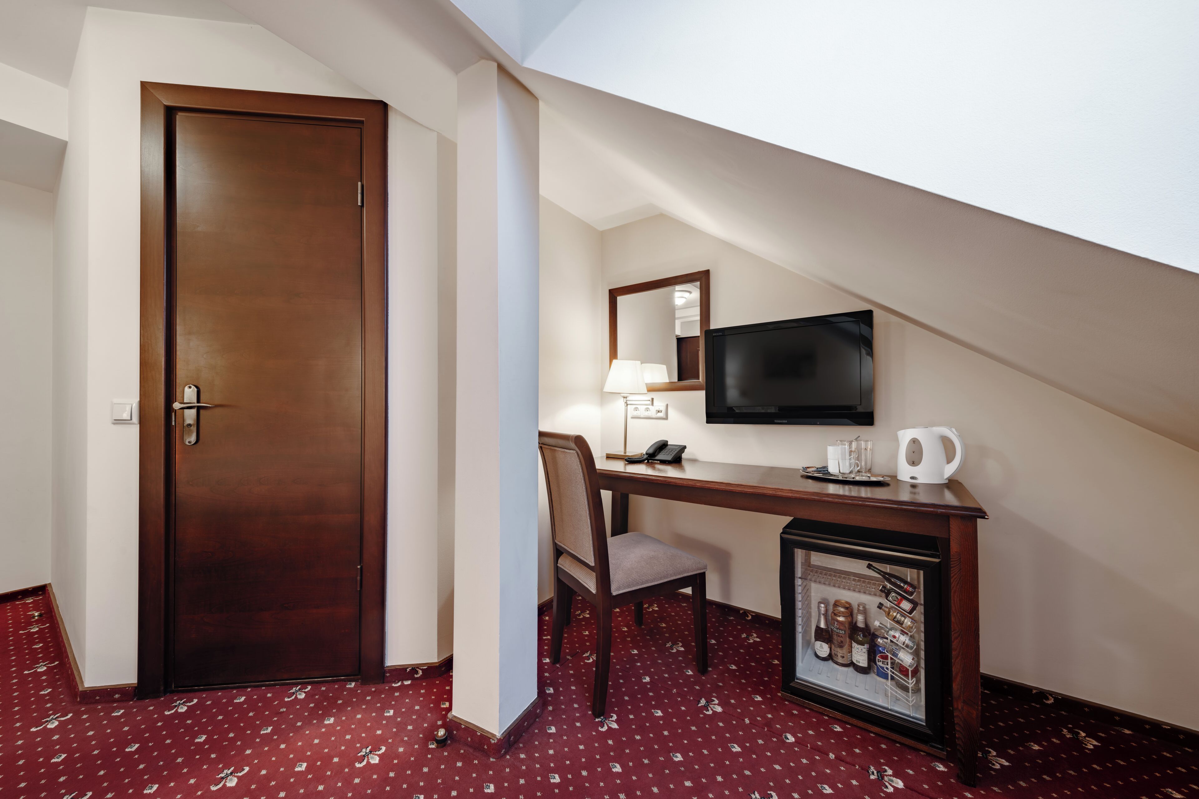 Una habitación de hotel con puerta de madera, un escritorio con silla, televisor y un minibar.
