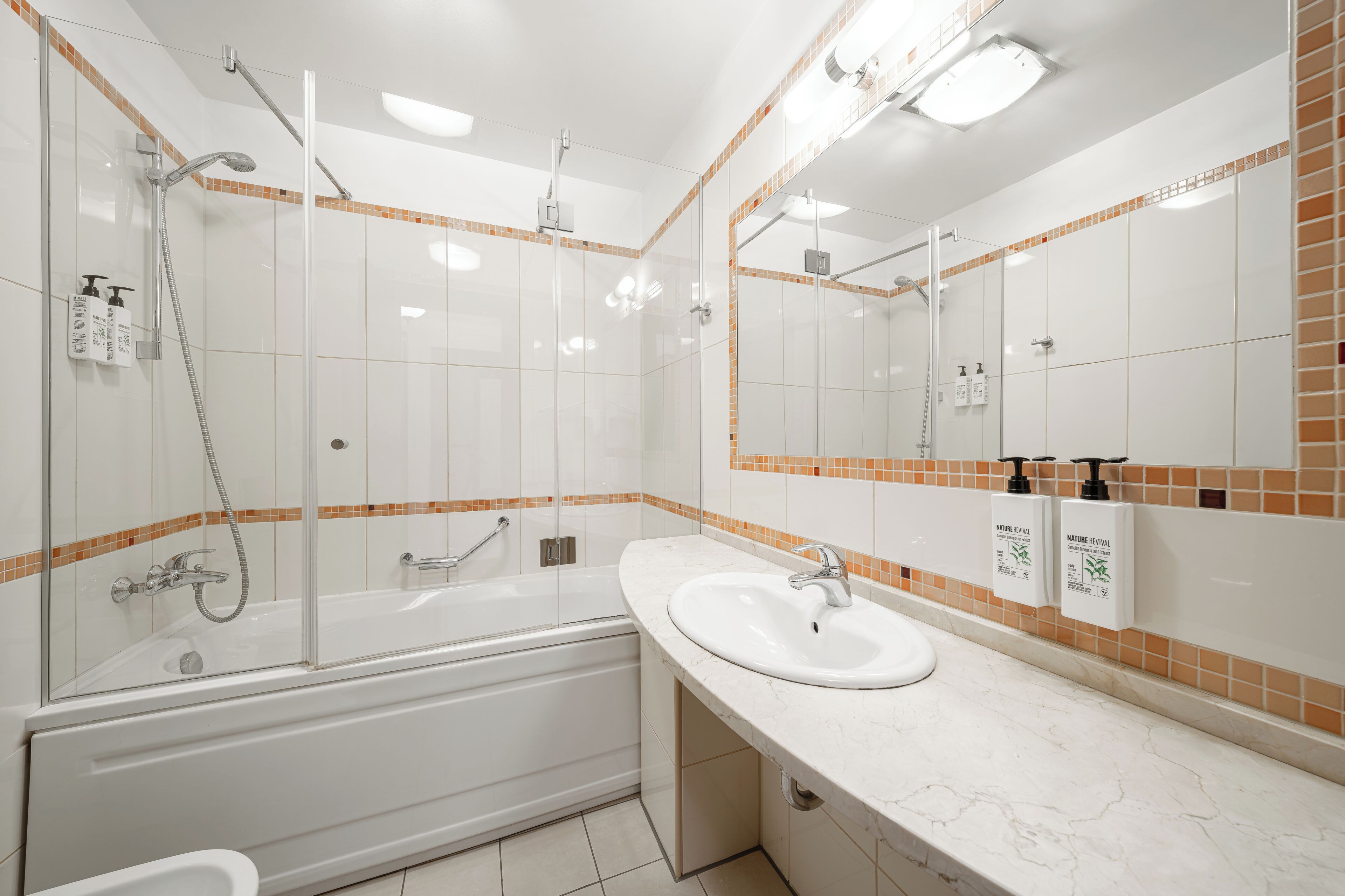 Une salle de bain moderne avec une douche à parois de verre, une baignoire sur pieds, un lavabo avec un miroir et des articles de toilette fixés au mur.